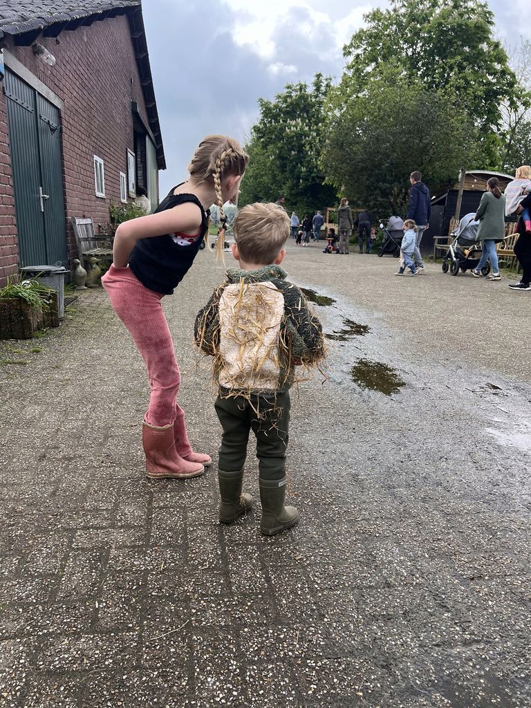 Kinderen in laarzen en met stro op hun kleren op het boerenerf