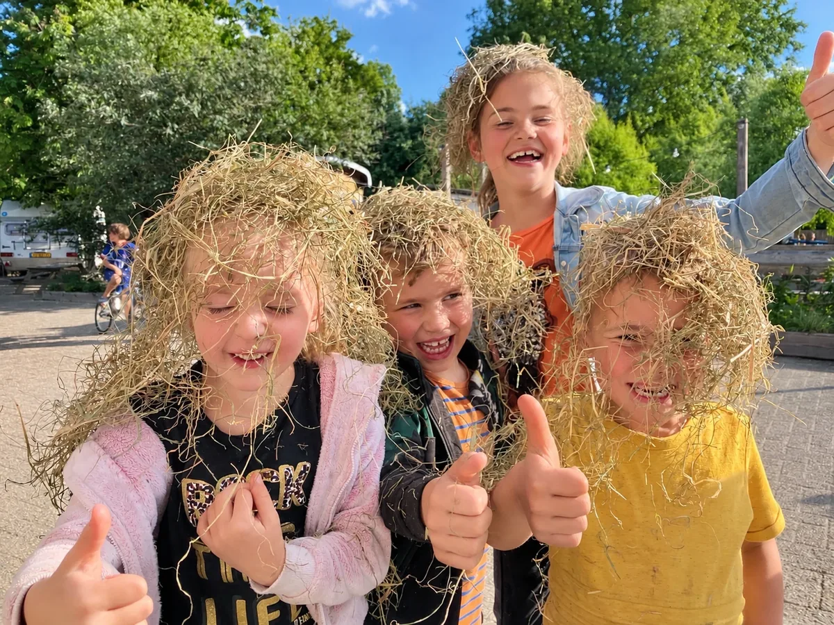 Kinderen met stro in hun haar en duimen omhoog op het erf