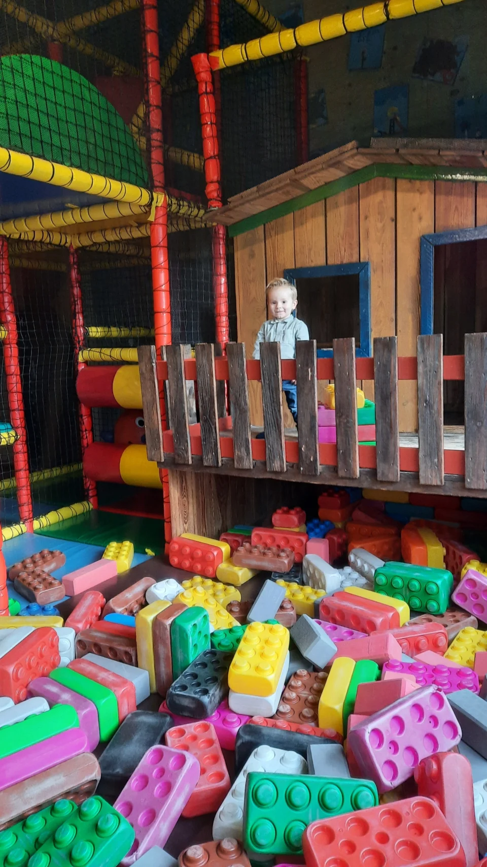 Een peuter staat in het speelhuisje van de binnenspeeltuin, met grote zachte blokken eronder.